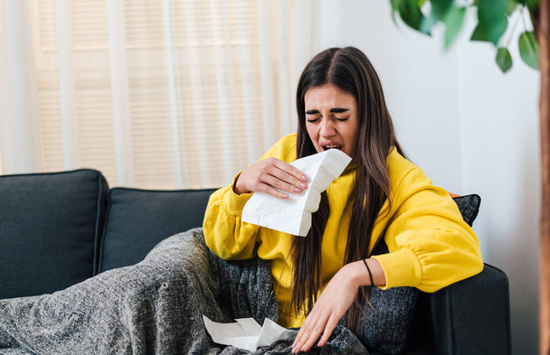 Ill young brunette woman in yellow sweatshirt, wiping her stuffy nose with paper towel. - Fotoğraf, Görsel