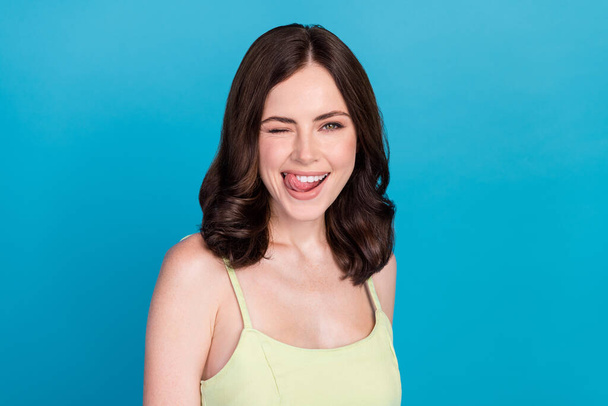 Photo of sweet tricky girl dressed green dress licking lips winking smiling isolated blue color background. - Foto, Bild