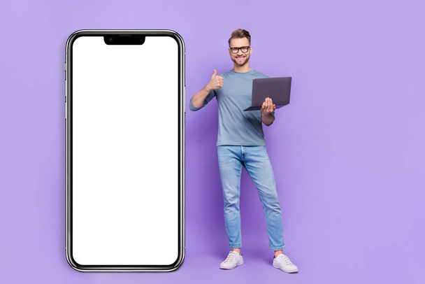 Photo of cheerful confident guy wear grey shirt typing modern device empty space thumb up isolated violet color background. - Photo, image