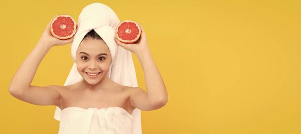 веселый ребенок в полотенце с грейпфрутом на желтом фоне. Косметика и уход за кожей для подростка, дизайн плакатов. Баннер с изображением девушки-красавицы - Фото, изображение