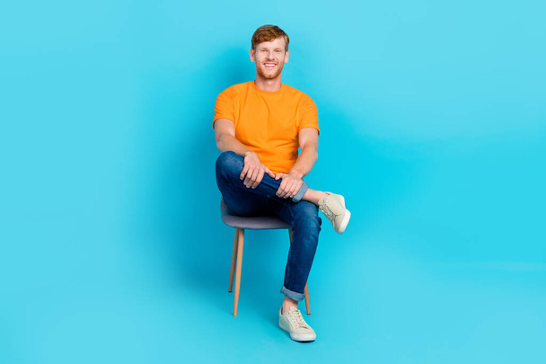 Fénykép a bájos édes férfi viselni narancssárga póló ülő iroda szék elszigetelt varangy szín háttér. - Fotó, kép