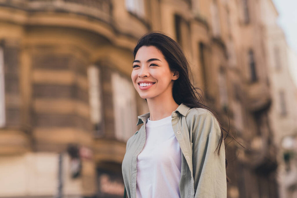 Photo of adorable shiny young asian woman wear khaki shirt enjoying fall sunshine walking city tour outside urban city street. - Fotó, kép