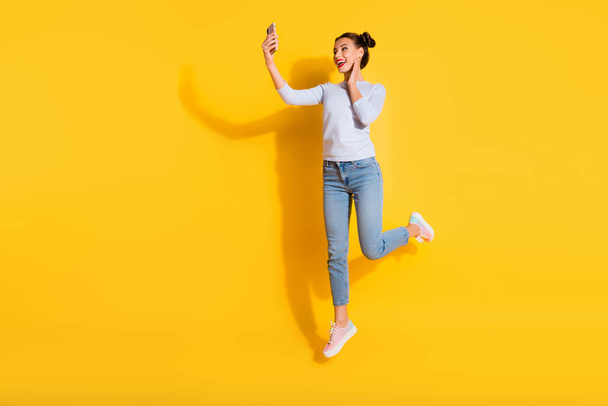 Full length photo of excited pretty lady wear long sleeve jumping high tacking selfie modern device isolated yellow color background. - Foto, Imagem