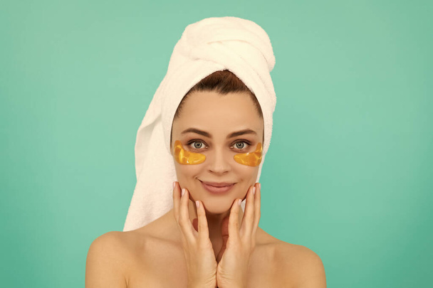 cheerful woman has collagen golden eye patches on face with towel. - Photo, Image
