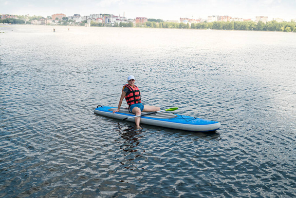 Молода жінка носить Життєвий жилет на Paddle Board після першої тренувальної сесії. спосіб життя в спекотний літній день - Фото, зображення