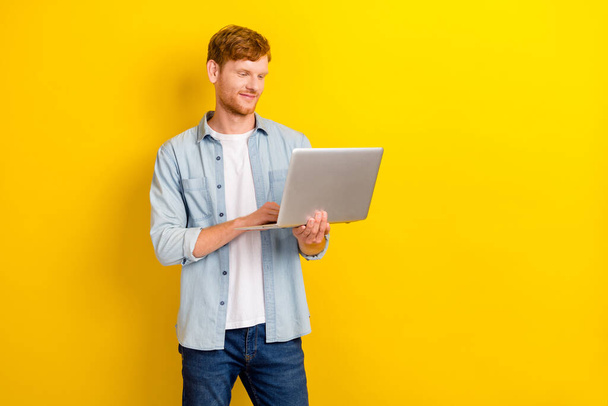 Photo portrait of charming young guy hold laptop coding test use new software wear stylish jeans outfit isolated on yellow color background. - Фото, зображення