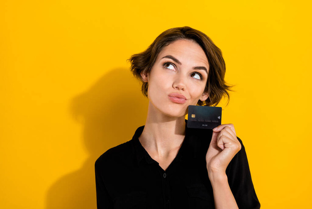 Photo of funky doubtful girl dressed formal shirt holding bank card looking empty space isolated yellow color background. - Valokuva, kuva