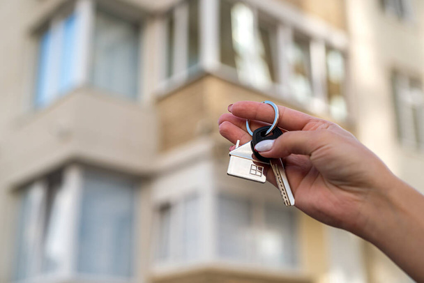Kulcs a ház kezében egy nő hátterében egy új lakás épület. ingatlankoncepció - Fotó, kép