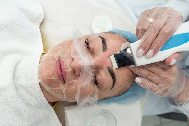 esthéticienne avec un pinceau applique un masque photochimique et glycolique sur le visage d'une patiente dans une clinique de beauté. le concept de procédures de beauté. salon de beauté. procédures de traitement - Photo, image
