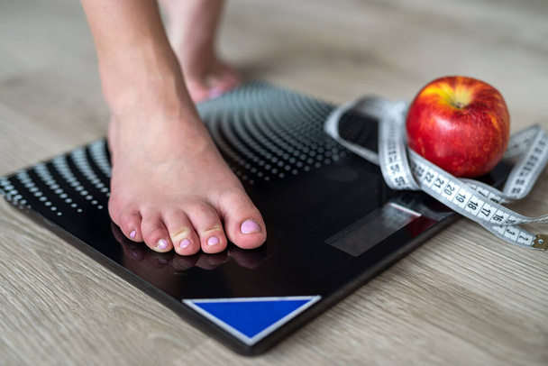  imagen de las piernas de una mujer de pie en escamas y una cinta métrica y una manzana cerca en el centro de la sala. medidas de peso. pies femeninos - Foto, imagen