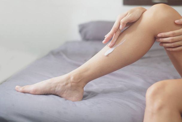 Asia mujer sentada en la cama y la aplicación de crema en su pierna. - Foto, imagen