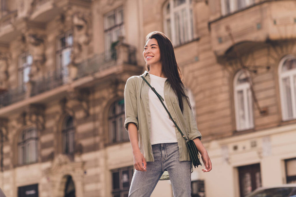 Photo of positive shiny young asian woman wear khaki shirt enjoying summer sunshine walking outside urban city street. - Zdjęcie, obraz