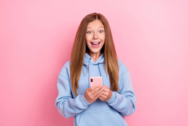 Photo of young funny excited girl wear blue hoodie hold smartphone reaction unexpected blogger youtube much followers isolated on pink color background. - Fotó, kép