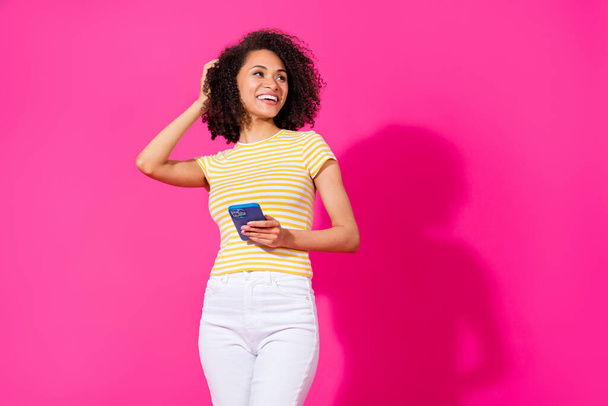Photo of charming young lady hold telephone look empty space dressed stylish yellow striped clothes isolated on shine pink color background. - Foto, Imagem