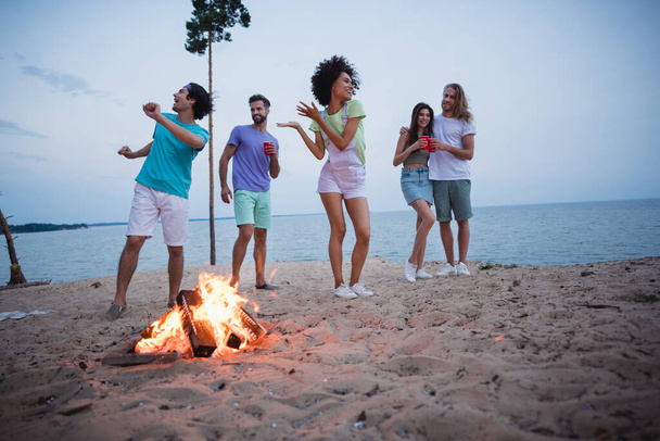 Full body photo of young guys ladies drink beer dance near fire wear casual cloth by the beach. - Fotoğraf, Görsel