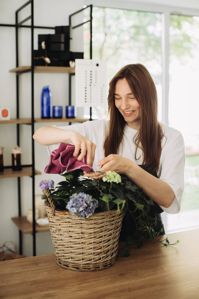 Eine junge Frau kümmert sich um Blumen. Eine fröhliche Floristin pflegt Blumen in einem Blumenladen. Konzept der Garten- und Floristik - Foto, Bild