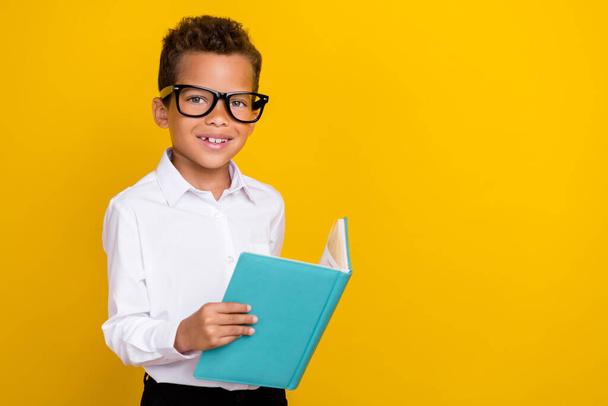 Photo of clever cute boy learner wear eyeglasses hold copybook read task question exercise empty space isolated on yellow color background. - 写真・画像