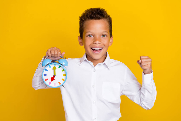 Photo of small delighted person arm hold clock raise fist toothy smile isolated on yellow color background. - Foto, afbeelding