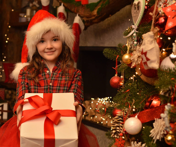 Sorrindo menina bonita em santa chapéu dá uma caixa com um presente no fundo da sala de Natal.clima de Natal - Foto, Imagem