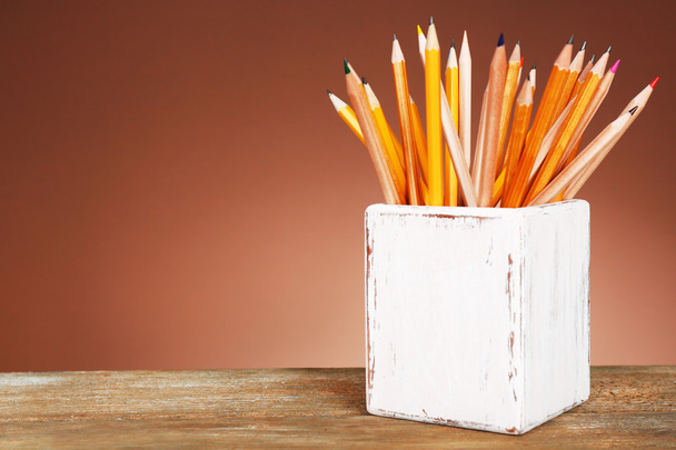 Holder with different pencils on wooden table and shaded color background - 写真・画像