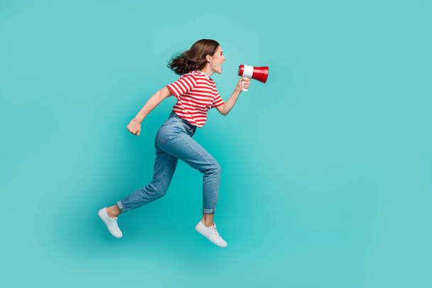 Full length photo of funky adorable lady wear striped t-shirt jumping high screaming speaker empty space isolated turquoise color background. - Foto, Imagen