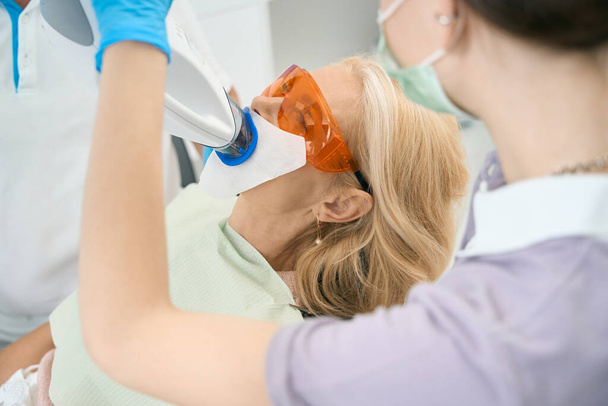 Procedimento de clareamento dos dentes que ocorre em um escritório moderno com equipamento - Foto, Imagem