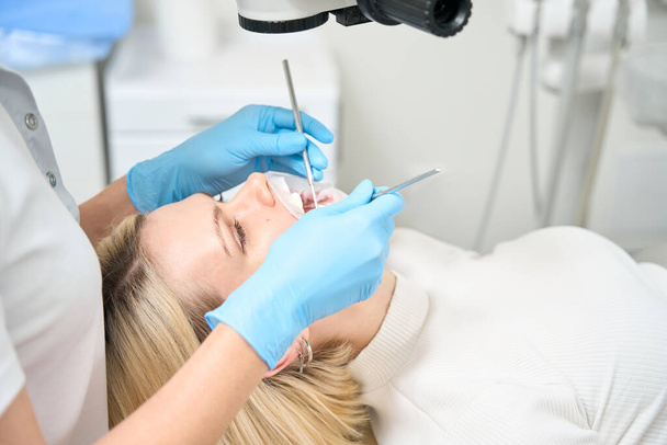 Woman dentist examines the oral cavity of a patient with a special tool - Foto, Bild