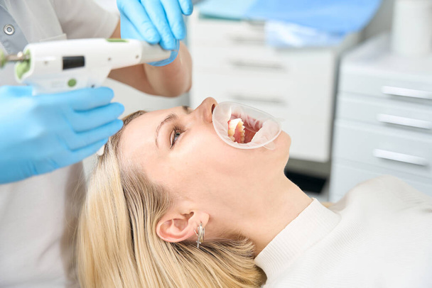 Felnőtt nő, fehér hajjal és nyitott szájjal fekszik egy szétterített fogászati klinikán - Fotó, kép