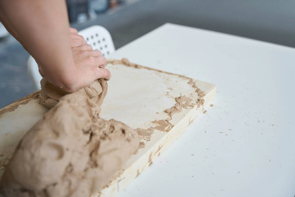 Craftswoman está trabalhando com um grande, pedaço macio de argila em uma placa de trabalho, suas mãos são sujas com argila - Foto, Imagem