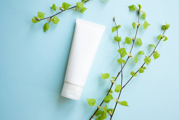 White Cream tube and birch branches with young small leaves on blue background. Cosmetic skincare product blank plastic package. White bottle of unbranded lotion, balsam, toothpaste mockup, flat lay. - Photo, Image