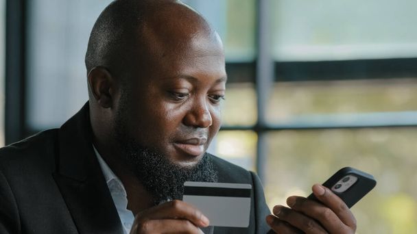 アフリカの顧客ビジネスマンがクレジットカードデータを入力電子マネー転送痛みのためのセキュリティコードを使用オンラインサービス携帯電話の銀行アプリで安全な支払い現代の技術は遠くに簡単に購入 - 写真・画像