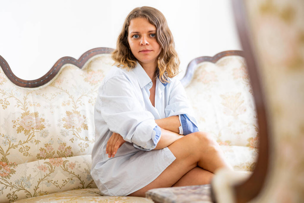 Portrait of attractive caucasian woman wearing mans shirt sitting on couch at home. - Foto, Imagem