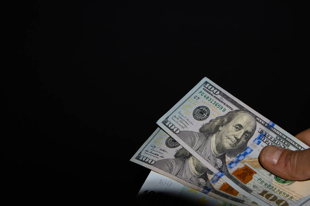 Mão direita detém pilha de duas notas de 100 dólares e notas de euro sobre fundo preto, a nota de 100 dólares é transferida à mão - Foto, Imagem