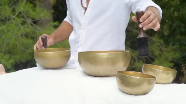 A man wearing in white doing healing sound massage with tibetan singing bowl, plaing with a wooden stick, stack over a singing Tibetan bowl during healing sound therapy, media shot - Footage, Video