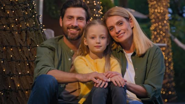 Happy Caucasian family portrait outdoors near lights. Close up smiling toothy mother bearded father and small girl daughter looking at camera custody adoption parents with kid child camping vacation - Footage, Video