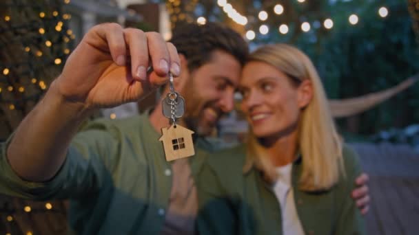 Portré szabadban kaukázusi boldog szerelmes pár házas házastársak ölelés ölelés bemutató csomó kulcsot az új ház ingatlan boldog vásárol lakás biztosítás otthon ül kívül fények - Felvétel, videó
