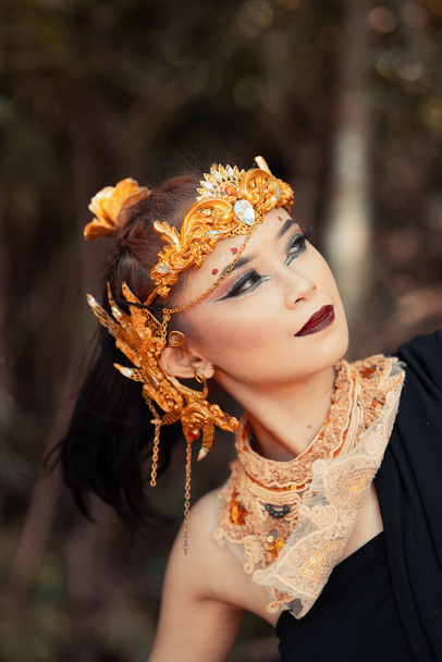Cara de cerca de una mujer asiática en maquillaje con corona de oro y accesorios de oro con hermosas caras dentro de la selva - Foto, imagen