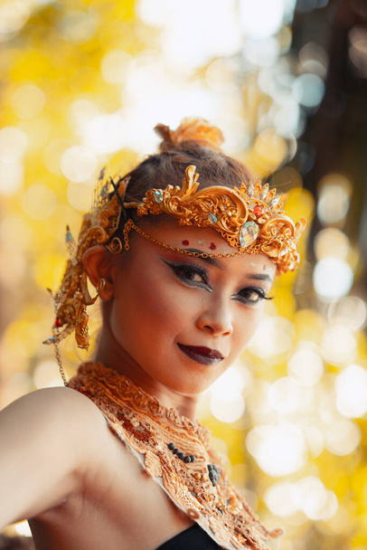 Portret Azjatki ubranej w złotą koronę i złoty naszyjnik ze swoim wspaniałym makijażem w czarnej sukience wewnątrz lasu - Zdjęcie, obraz