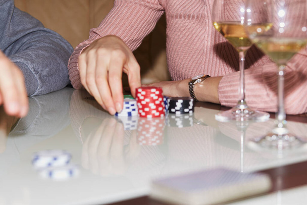 Woman holds playing chips in poker game. Cards, dices and glasess of champagne. Candid moment. Poker background lifestyle photography. Enjoying the moment, digital detox with friends - Photo, Image