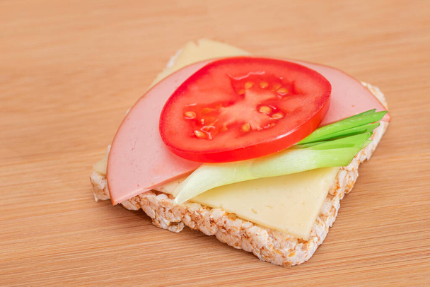 トマトとライスケーキサンドイッチ,ソーセージ,木製のまな板上の緑の玉ねぎとチーズ.簡単な朝食。ダイエット食品。迅速かつ健康的なサンドイッチ。おいしい充填とクリスピーパン.健康的な食事のスナック。 - 写真・画像