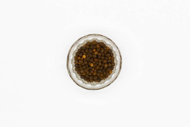 Black peppercorns in a glass pepper pot on a white background. Isolated. Spices and herbs for cooking healthy food. Kitchen accessory. Brown pepper seeds. traditional seasoning for meat and dishes. - Photo, Image
