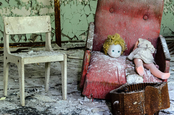 Sala de jogos num edifício Prypiat. Uma boneca decapitada está deitada em uma cadeira quebrada vermelha ao lado de um assento vazio. Zona de Exclusão de Chernobyl, Ucrânia. Foto de alta qualidade - Foto, Imagem