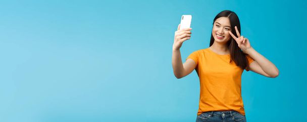 Freundlich fröhlich hübsche asiatische Frau brünett Kurzhaarschnitt Selfie machen, lächeln freudig halten Smartphone zeigen Frieden, Siegeszeichen am Handybildschirm vor der Kamera, reden Familie Video-Anruf. - Foto, Bild
