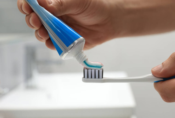 Man applying toothpaste on brush in bathroom, closeup - Photo, image