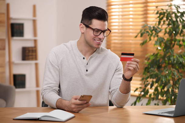 Uomo che utilizza smartphone e carta di credito per il pagamento online alla scrivania in camera - Foto, immagini