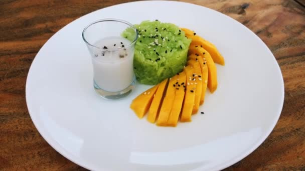 Witte schotel met rijstpap en rauwe rijpe zoete mango, bestrooid met sesamzaad en een drinkglas met rijstmelk - Video