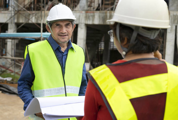 Mühendis kıdemli amiri, inşaat alanında çalışan iş mühendisi ve planlı mühendis meslektaşıyla sohbet ediyor. - Fotoğraf, Görsel