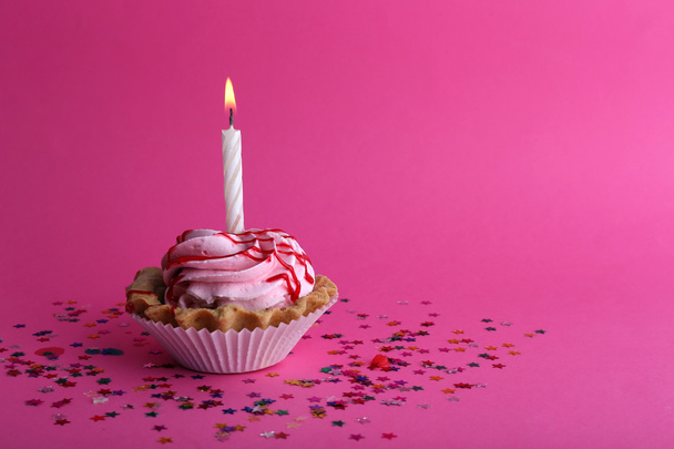 Birthday cup cake with candle and colorful stars on pink background - Photo, image