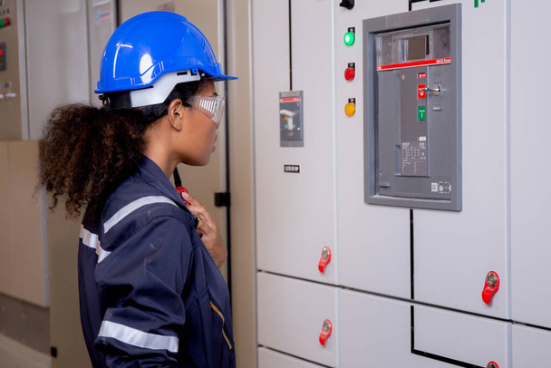 Electrical young asian woman engineer examining maintenance cabinet system electric and using radio in control room at industrial factory, technician or electrician inspection power distribution. - Foto, Imagen