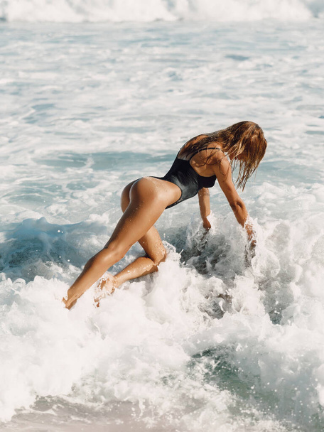 Mujer atractiva en traje de baño negro posando con olas del océano - Foto, imagen